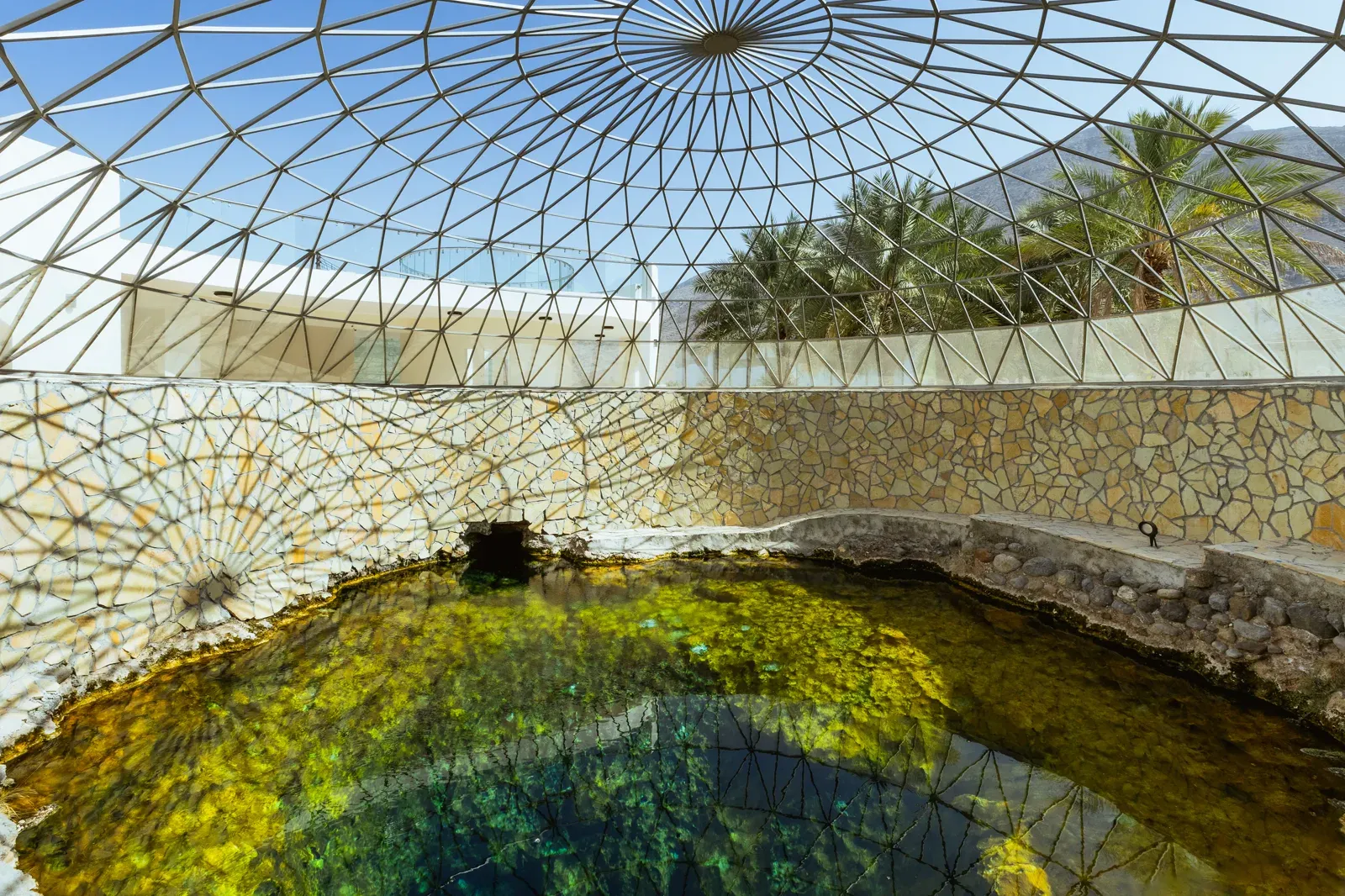 De overkoepelde warmwaterbron van Ain Al Kasfa bij Rustaq, met helder groen bronwater onder een fijnmazige glaskoepel