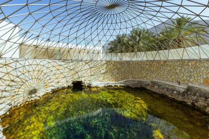 De overkoepelde warmwaterbron van Ain Al Kasfa bij Rustaq, met helder groen bronwater onder een fijnmazige glaskoepel