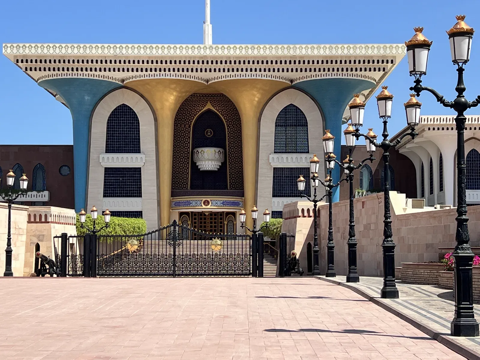 De blauw-gouden zuilengevel van het Al Alam Palace van dichtbij, met een rij sierlijke lantaarnpalen langs het ceremoniële plein