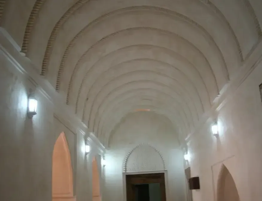Een lange gepleisterde gang in het Al Hazm-fort met een geribbeld tongewelf en sierlantaarns langs de wanden