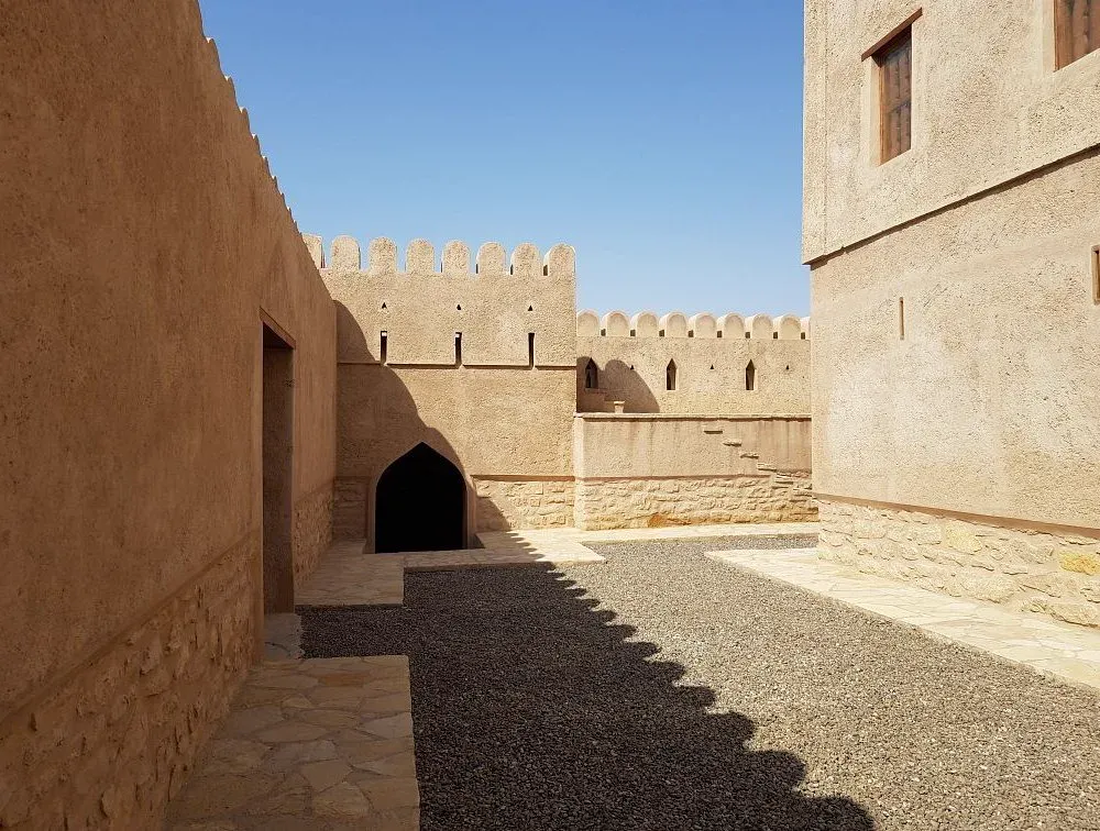 Een binnenplaats van Al Hillah Fort met hoge lemen muren, gekanteelde borstwering en een spitsbogige doorgang