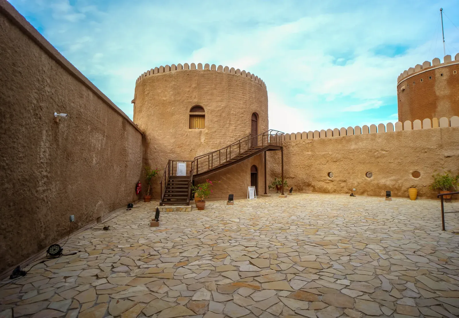 De geplaveide binnenplaats van Al Mirani Fort met de massieve ronde toren en kantelen tegen een blauwe lucht