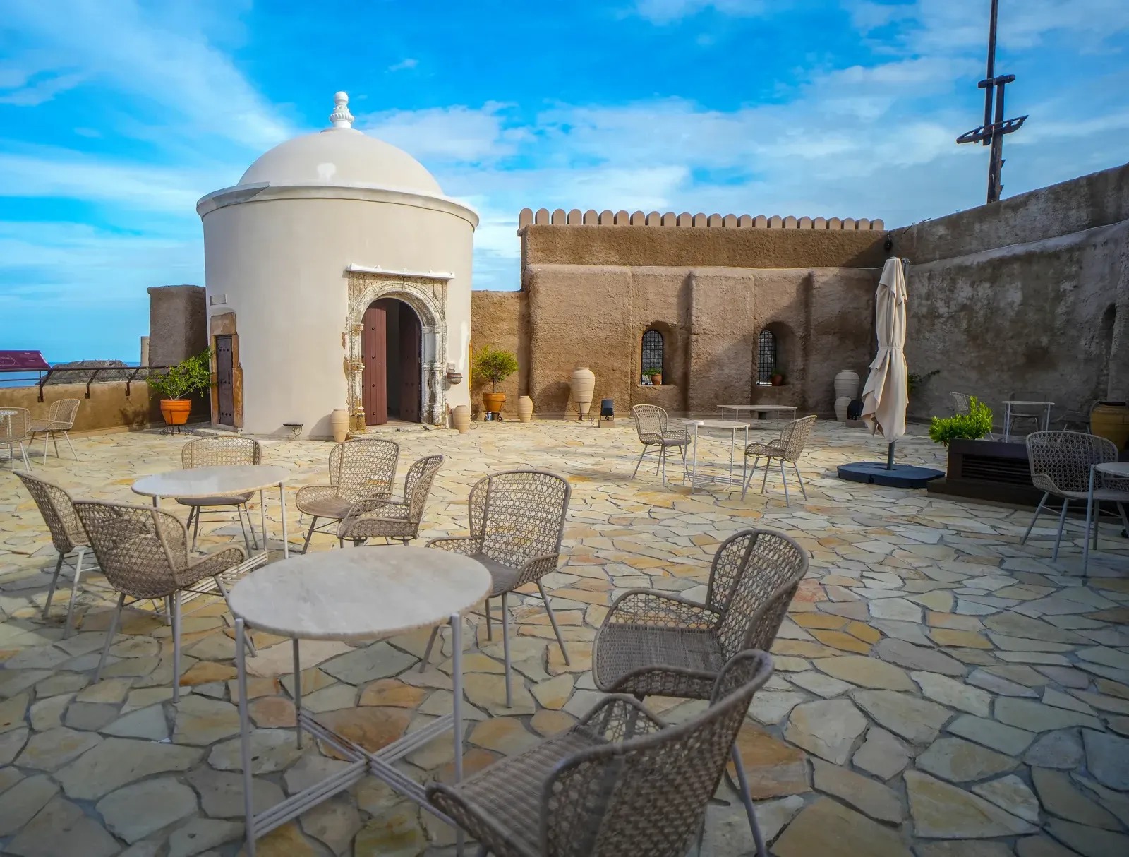 Het dakterras van Al Mirani Fort met cafétafels en een witte koepel, uitkijkend over de Zee van Oman