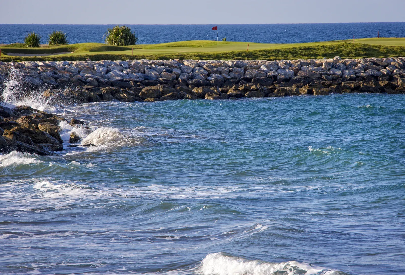 Een green van Al Mouj Golf pal aan de oceaan, begrensd door een rotskust en helderblauw water