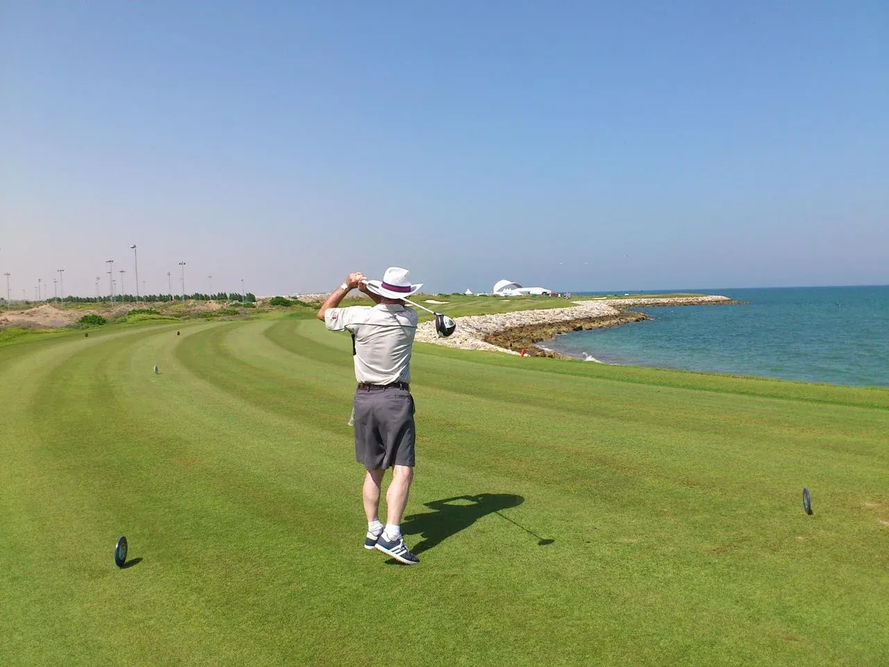 Een golfer slaat af op Al Mouj Golf, waar de fairway direct langs de kustlijn van de oceaan loopt