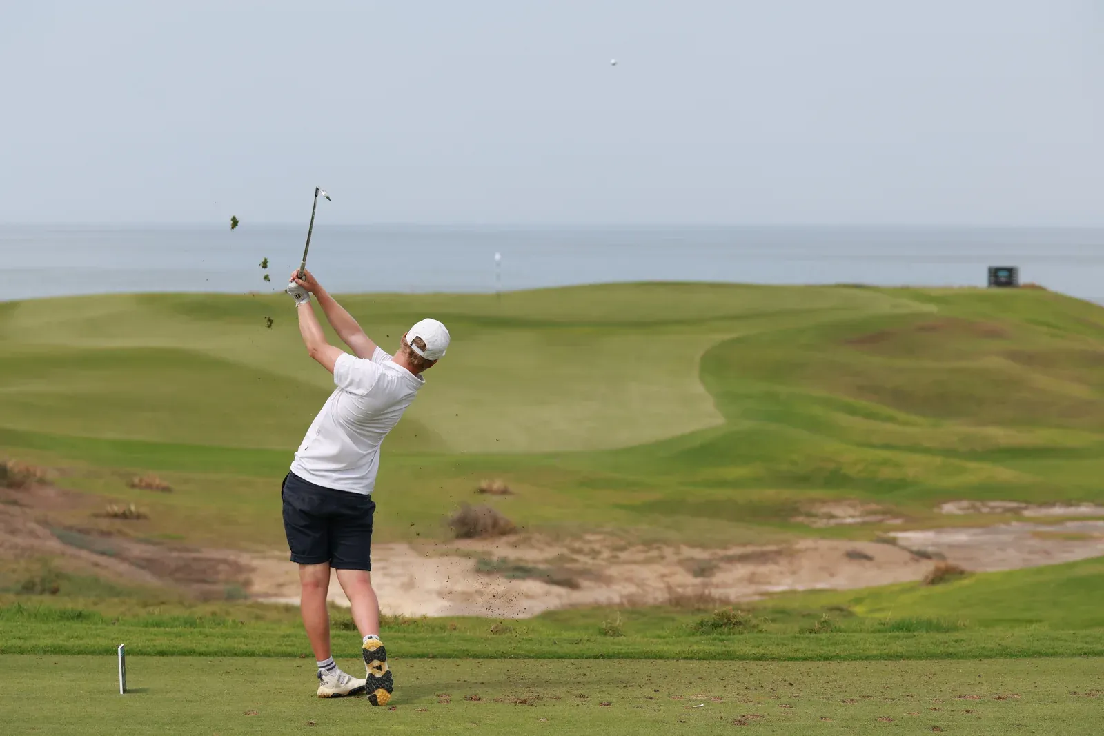 Een golfer maakt een swing op Al Mouj Golf, met de glooiende fairway en de kust op de achtergrond