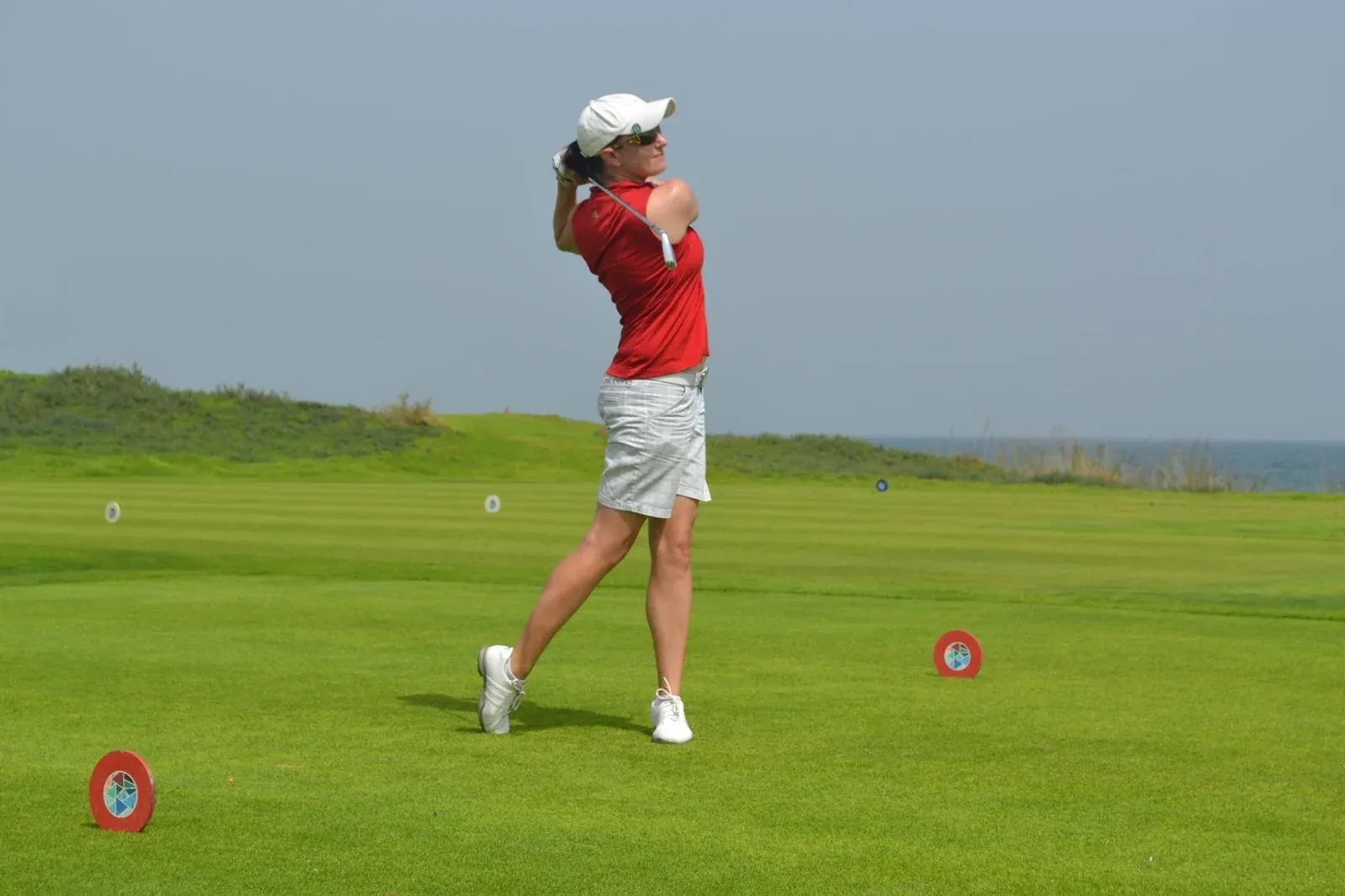 Een golfster slaat af op de linksbaan van Al Mouj Golf, met de zee op de achtergrond