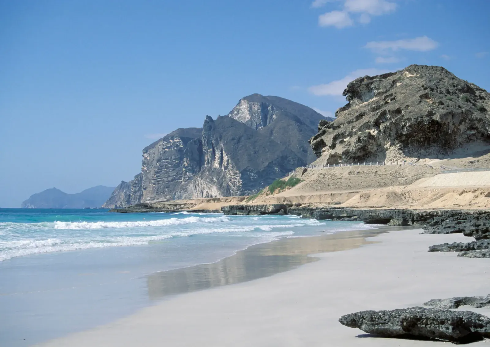 Het witte zandstrand van Al Mughsail bij Salalah met turquoise branding en dramatische kalkstenen kliffen op de achtergrond