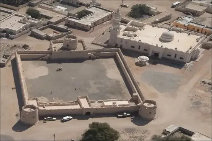 Luchtfoto van het vierkante Al Sunaysilah Fort met zijn vier hoektorens en open binnenplaats, naast een moskee in Sur