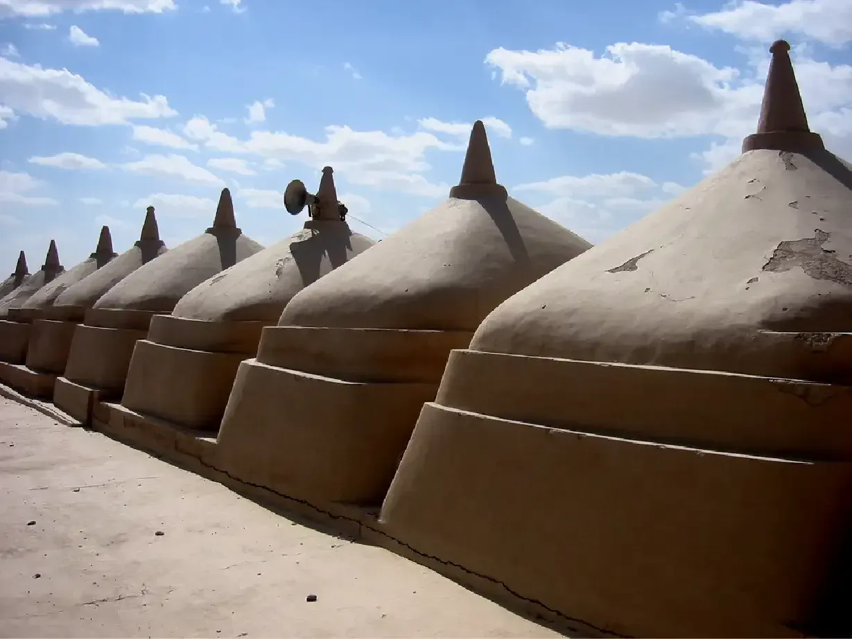 De rij lemen koepels op het dak van de Alqubab-moskee in Jalan Bani Bu Ali, scherp aflopend tegen een blauwe lucht met wolken