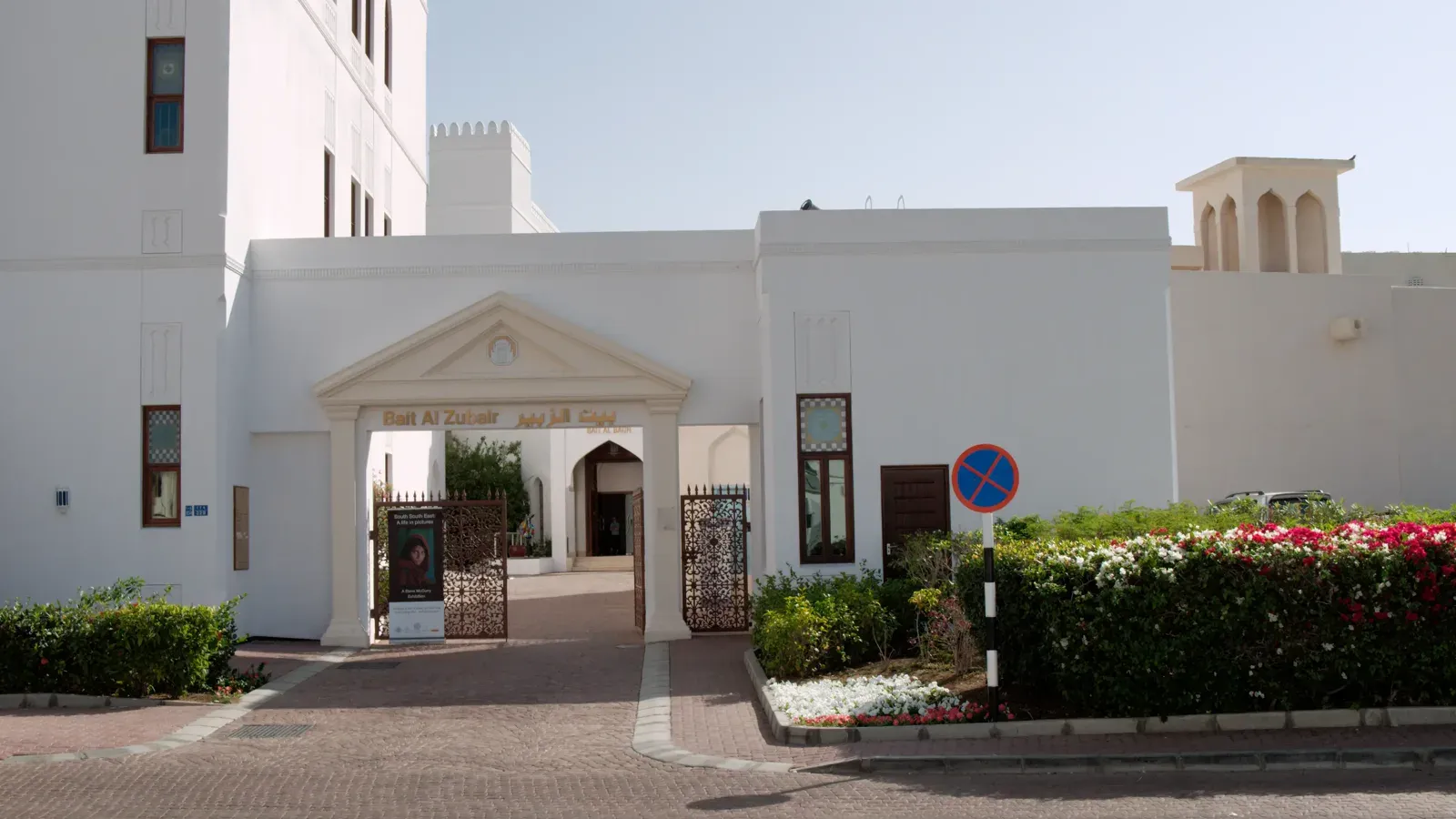De witte hoofdingang van het Bait Al Zubair Museum in oud Muscat, met bloeiende borders
