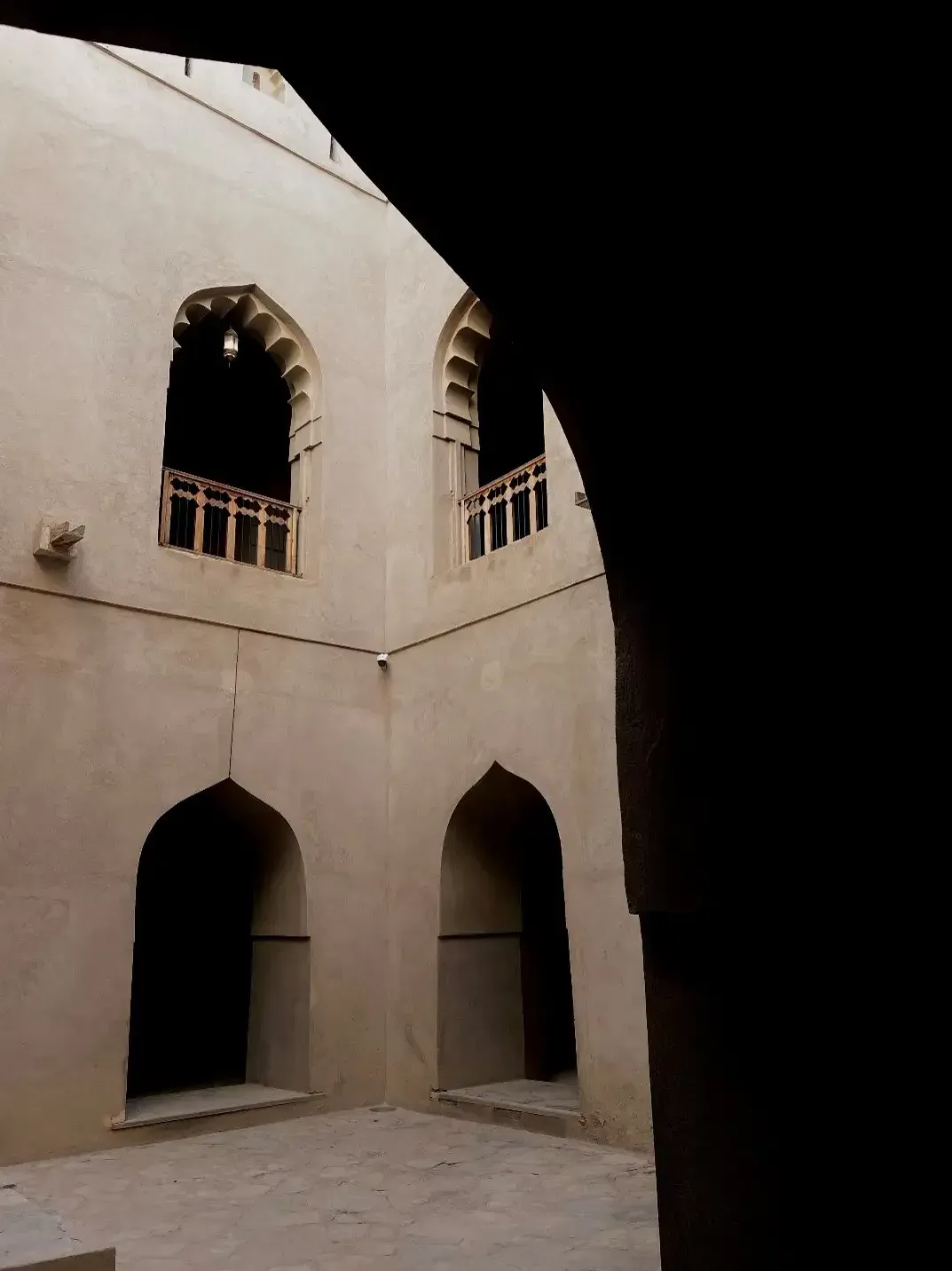 Een sfeervolle binnenplaats in Bayt Ar-Ridaydah met sierlijke spitsbogen en een houten balustrade in het zachte licht