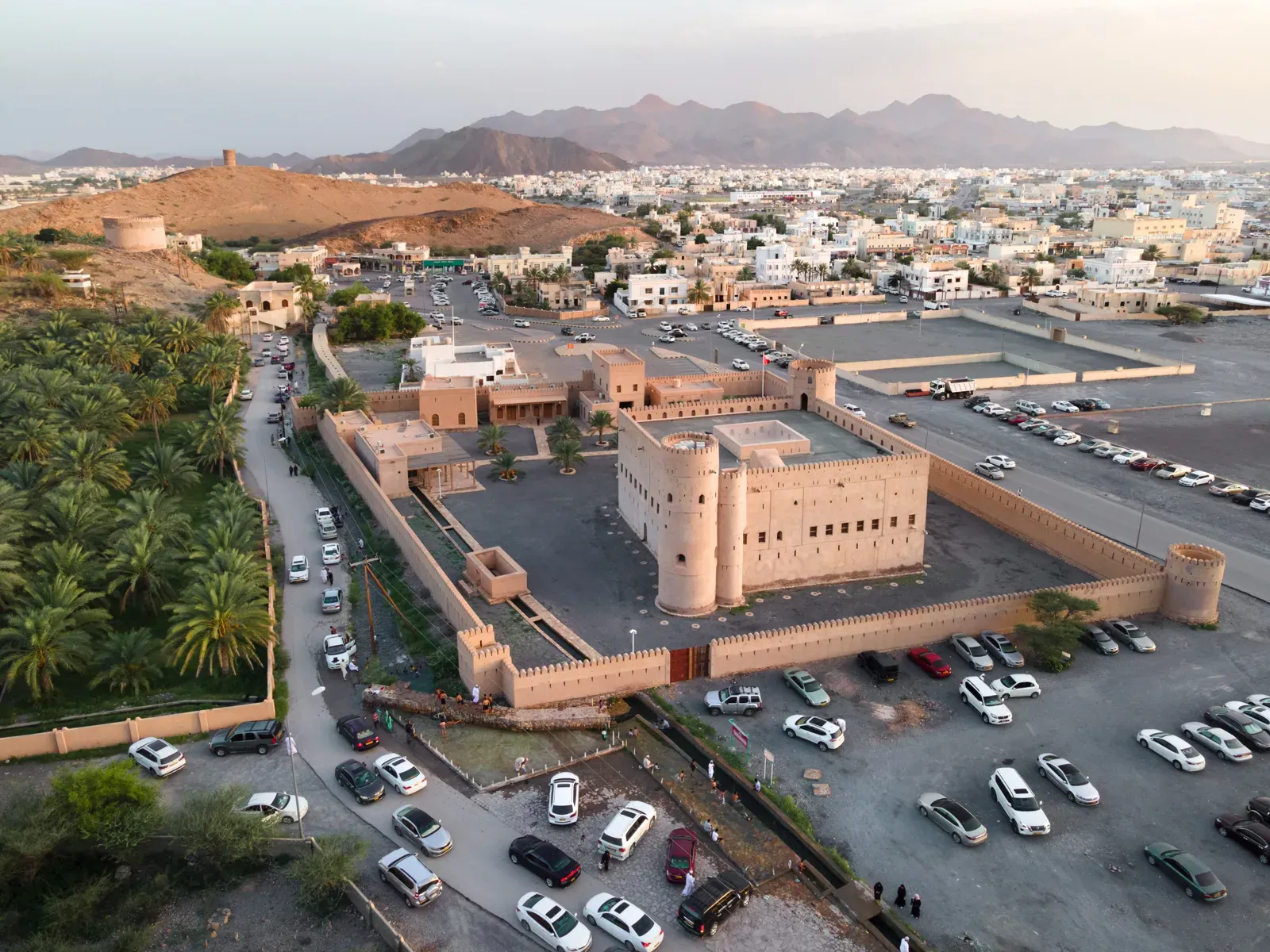 Luchtfoto van het versterkte huis Bayt Ar-Ridaydah bij Nizwa, met zijn verdedigingsmuur en hoektorens aan de voet van de bergen