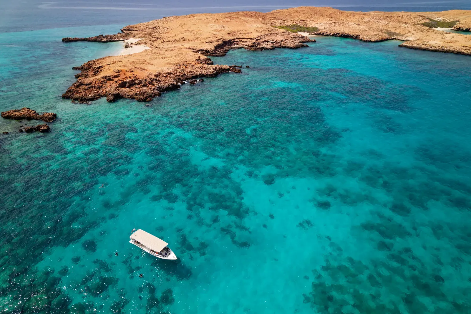 Luchtfoto van de Daymaniyat-eilanden met koraalriffen die door het kristalheldere turquoise water schemeren en een bootje voor de kust