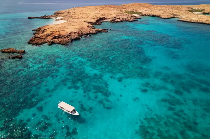 Luchtfoto van de Daymaniyat-eilanden met koraalriffen die door het kristalheldere turquoise water schemeren en een bootje voor de kust