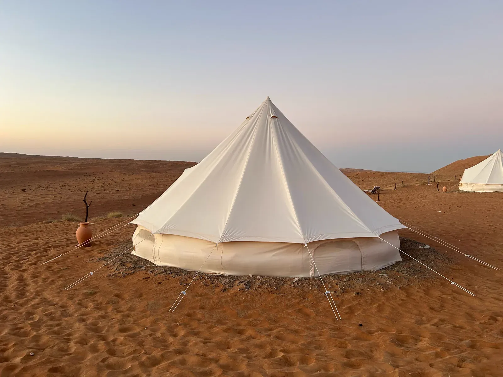 Een ruime witte glamping-belttent in de woestijn van de Wahiba bij avondlicht, met de duinen op de achtergrond