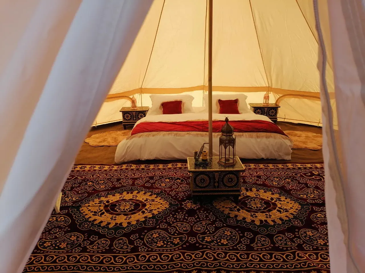 Het luxueuze interieur van een glamping-tent met een tweepersoonsbed, lantaarn en kleurrijke Omaanse tapijten