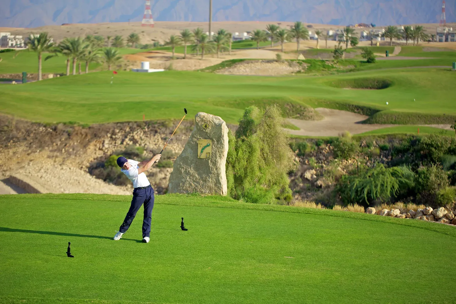 Een golfer slaat af tussen de bunkers en palmen van de Muscat Hills-golfbaan