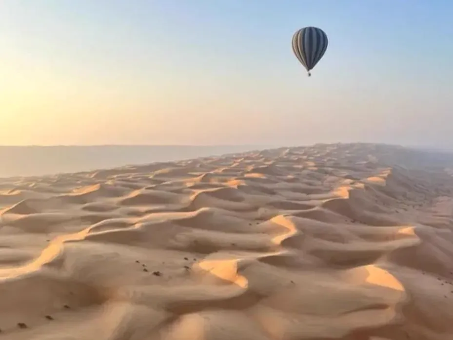 Een heteluchtballon zweeft bij zonsopkomst over de eindeloze, zachtgolvende duinen van de Wahiba Sands