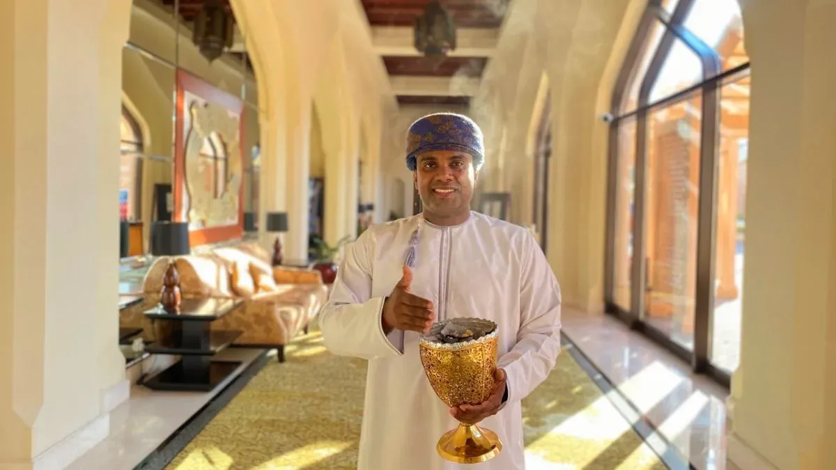 Man in traditionele Omaanse kleding met een gouden wierookbrander in een lichte hotelgang