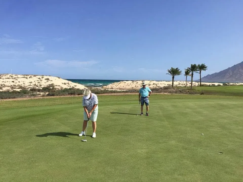 Twee golfers op de fairway van Jebel Sifah Golf, tussen de duinen en palmen aan zee