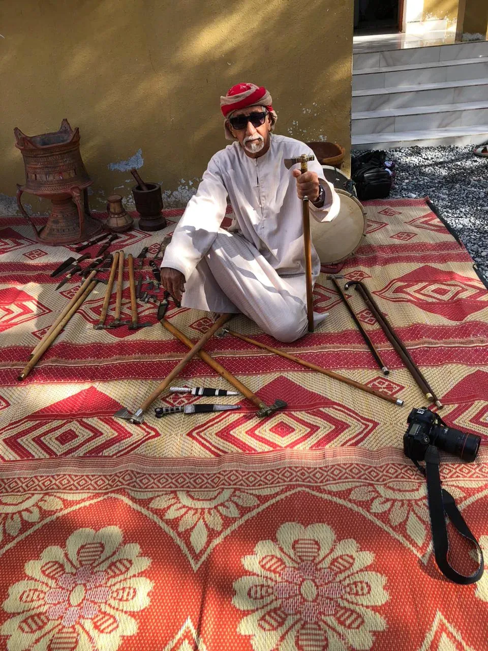 Een Omaanse verkoper toont traditionele wandelstokken, aardewerk en khanjars op een rood kleed