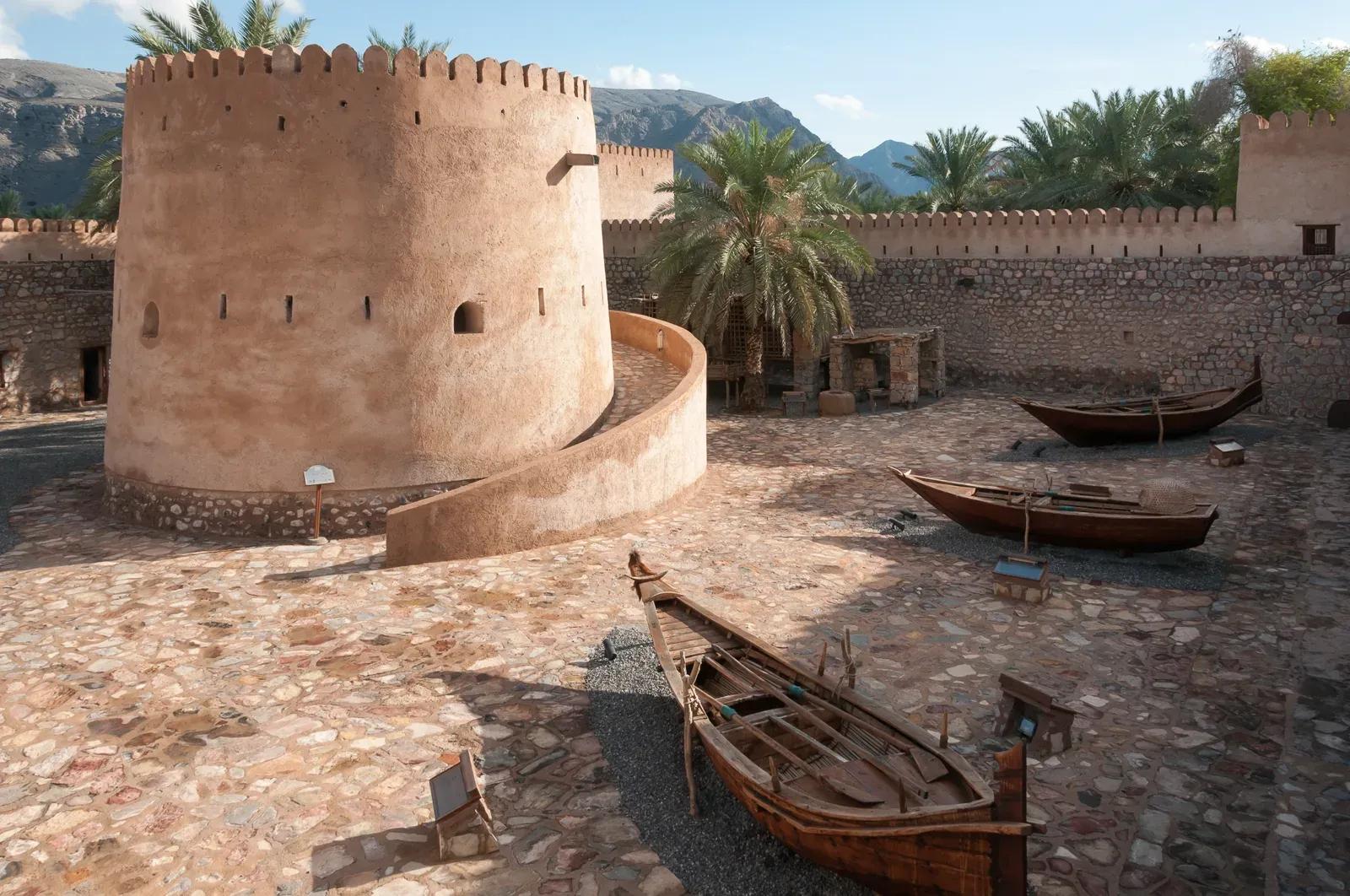 De binnenplaats van Khasab Fort met de ronde centrale toren en traditionele houten boten tegen een achtergrond van bergen