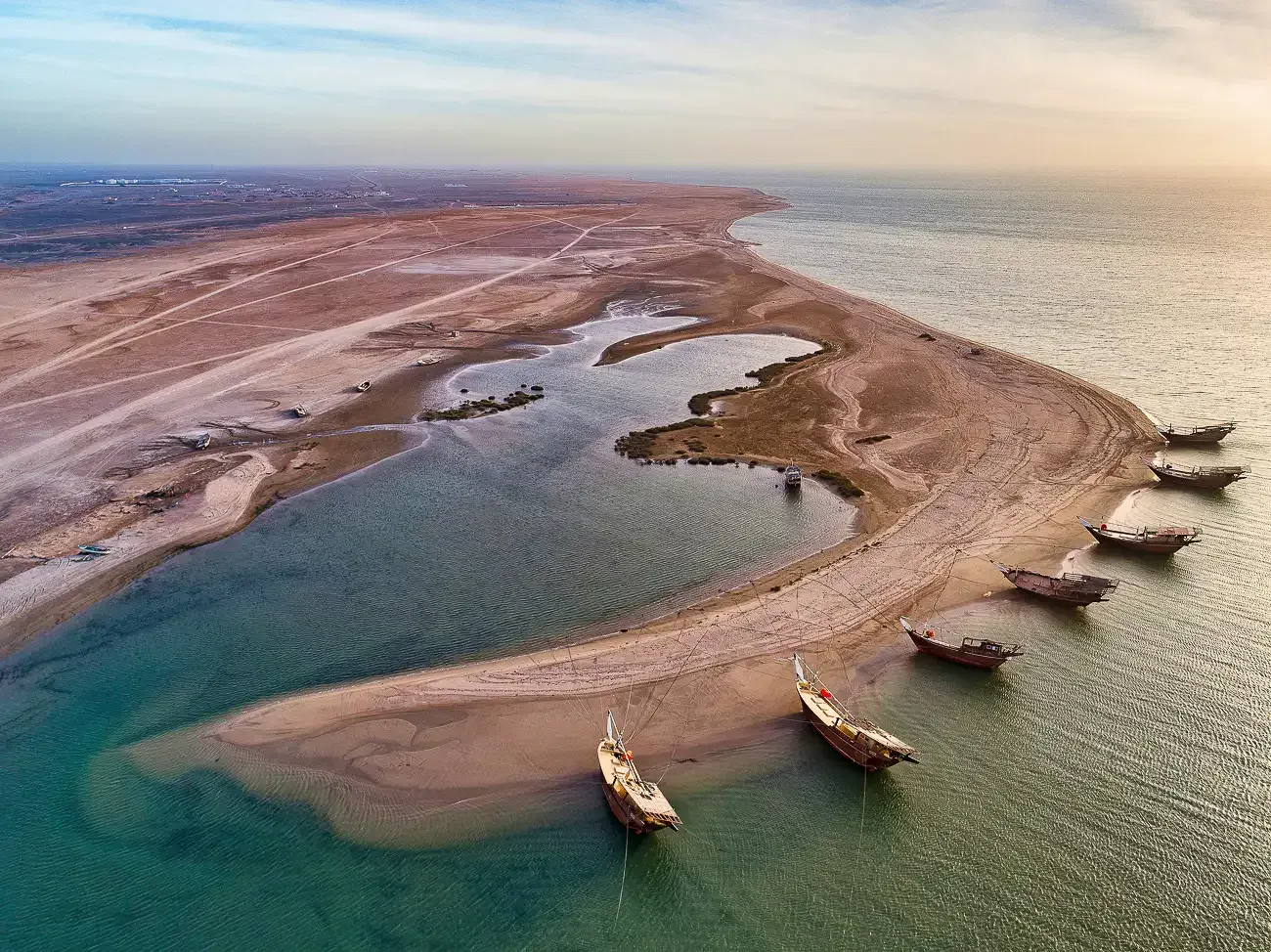 Luchtfoto van een zandtong van het eiland Masirah met lagunes, gestrande bootjes en de kalme zee in het avondlicht