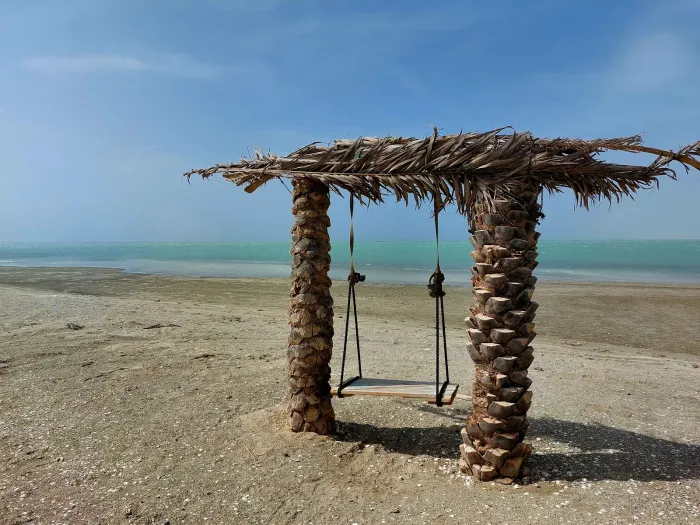 Een schommel tussen twee palmstammen op een verlaten strand van Masirah, met turquoise zee