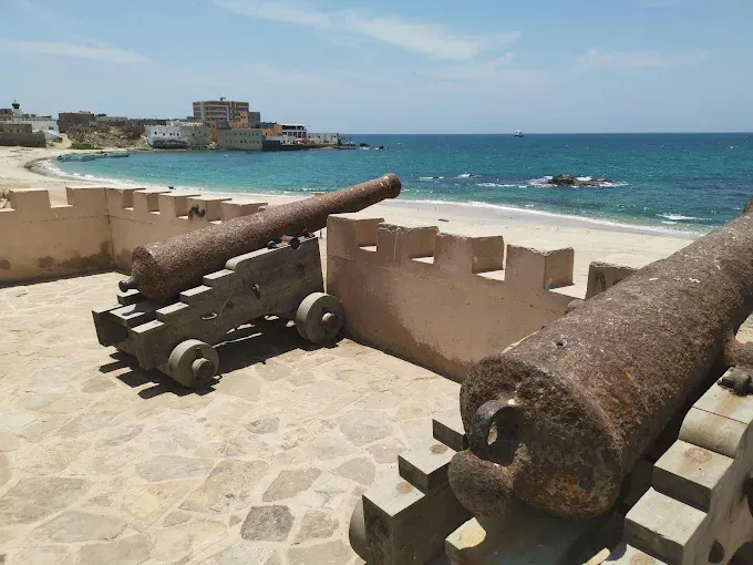 Oude kanonnen op de borstwering van Mirbat Castle, uitkijkend over het witte strand, de oude haven en de turquoise zee