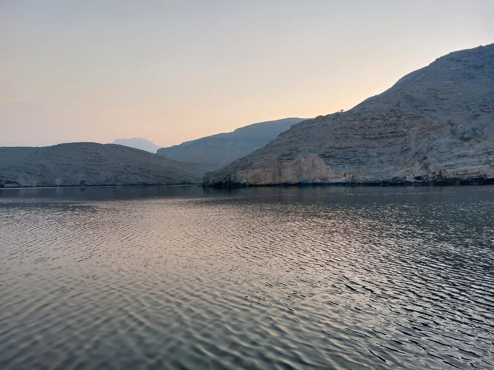 Zachtroze ochtendlicht over het stille water en de bergen van een Musandam-fjord