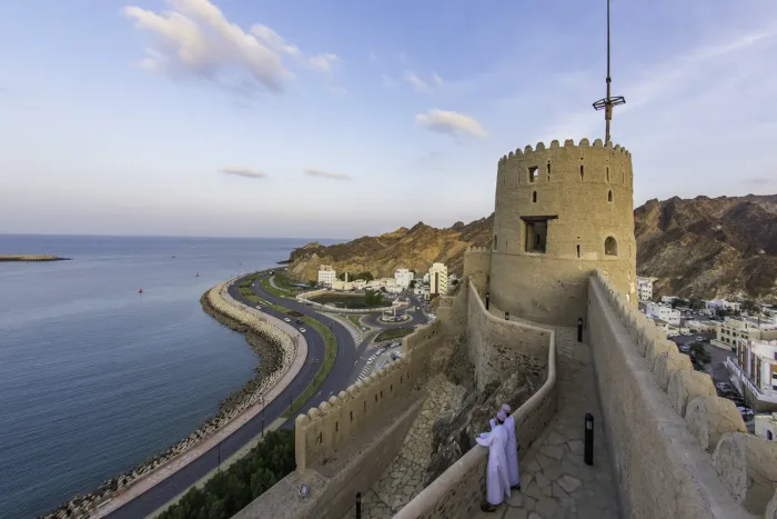 Het 16e-eeuwse Muttrah Fort op de heuvel boven de Corniche van Muscat, met de boog van de baai en de Hajar-bergen op de achtergrond