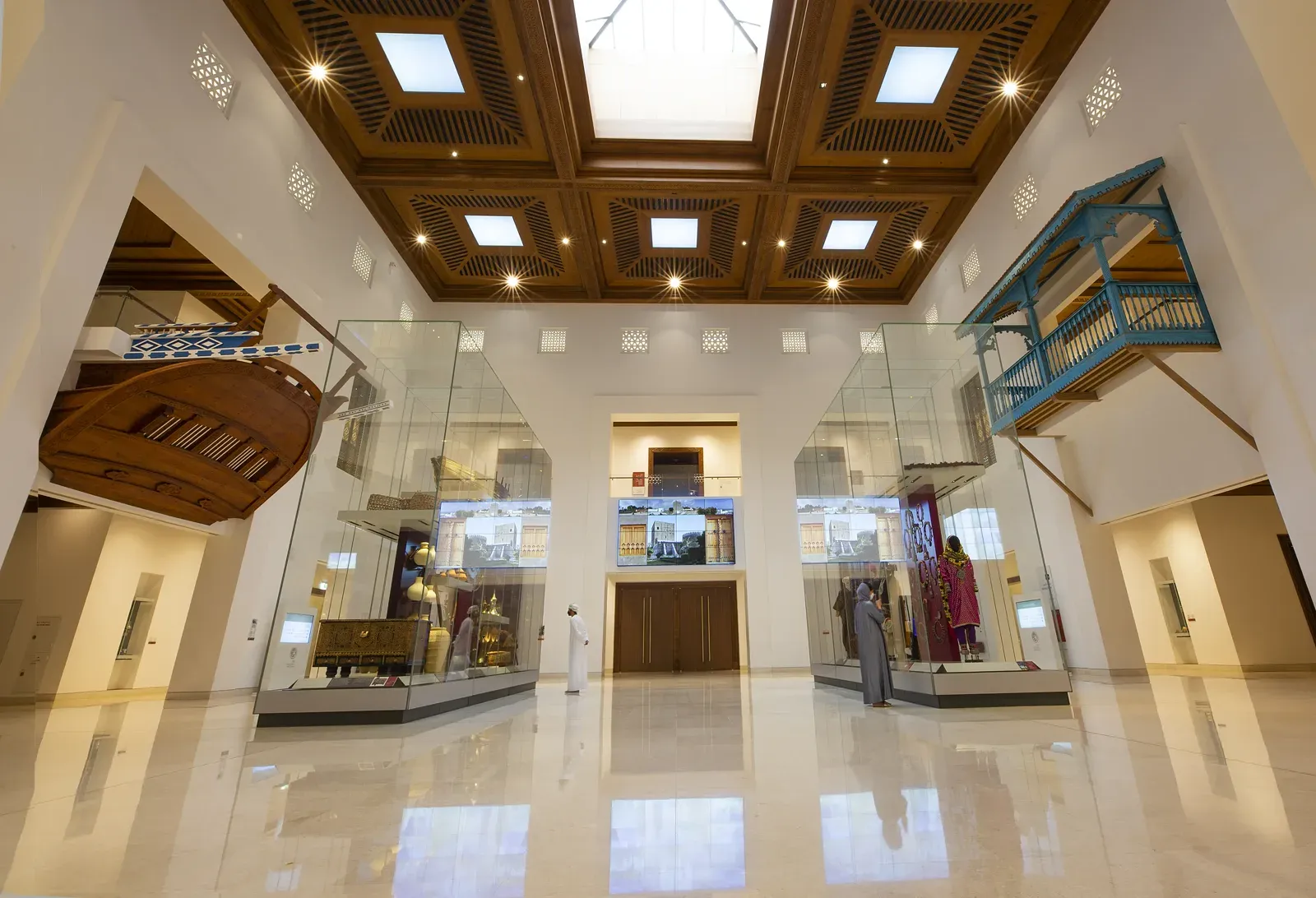 De ruime, lichte hal van het Nationaal Museum van Oman met glazen vitrines, een houten dhow en een fijn bewerkt cassetteplafond