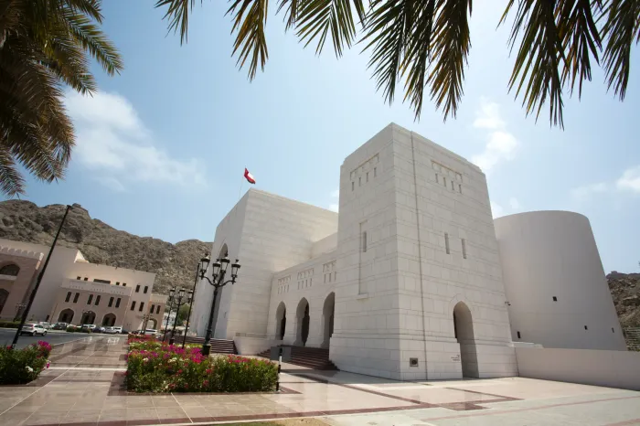 Het Nationaal Museum van Oman in lichte natuursteen in oud Muscat, met de Omaanse vlag en bloeiende bougainville onder palmen