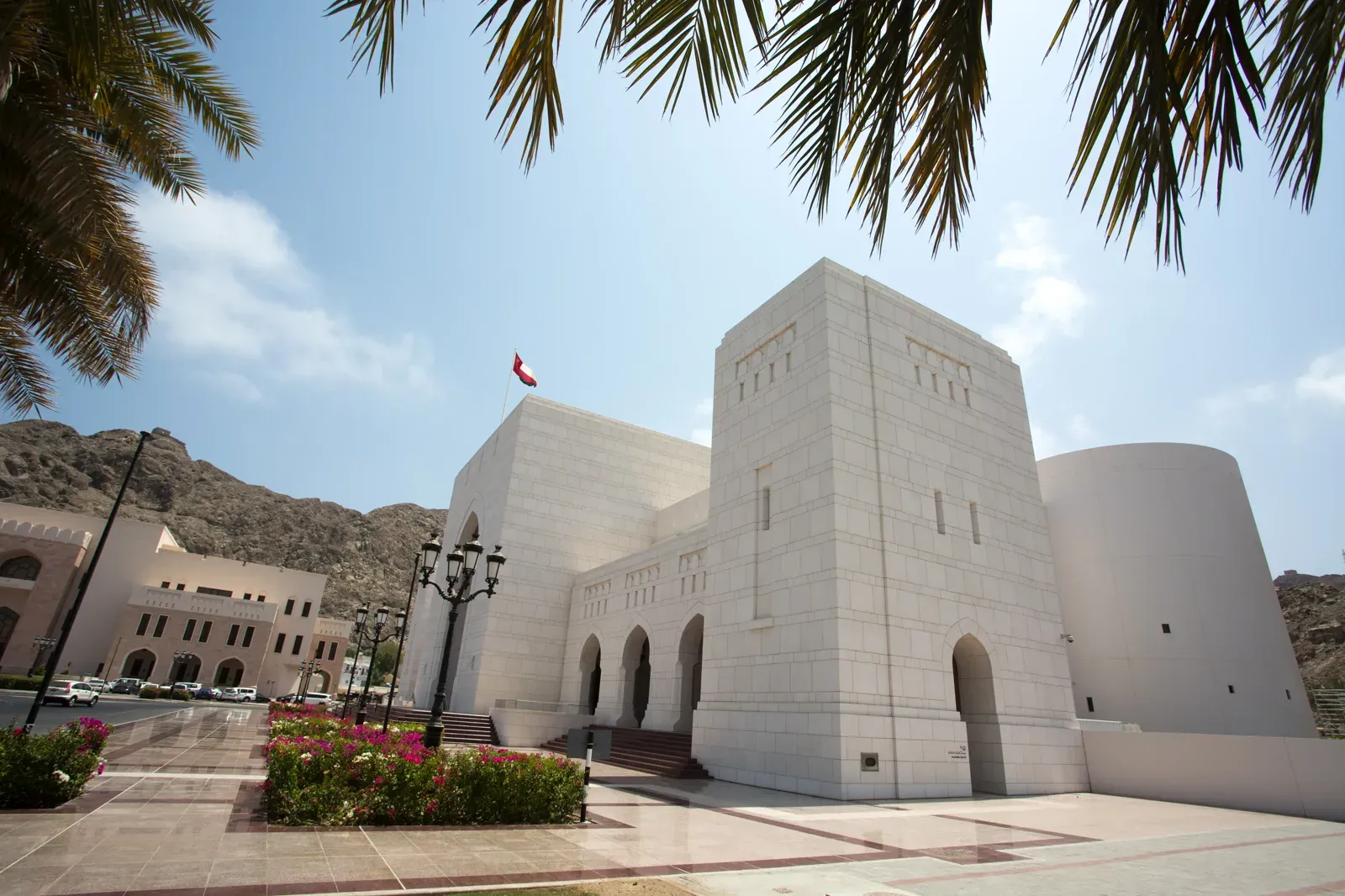Het Nationaal Museum van Oman in lichte natuursteen in oud Muscat, met de Omaanse vlag en bloeiende bougainville onder palmen