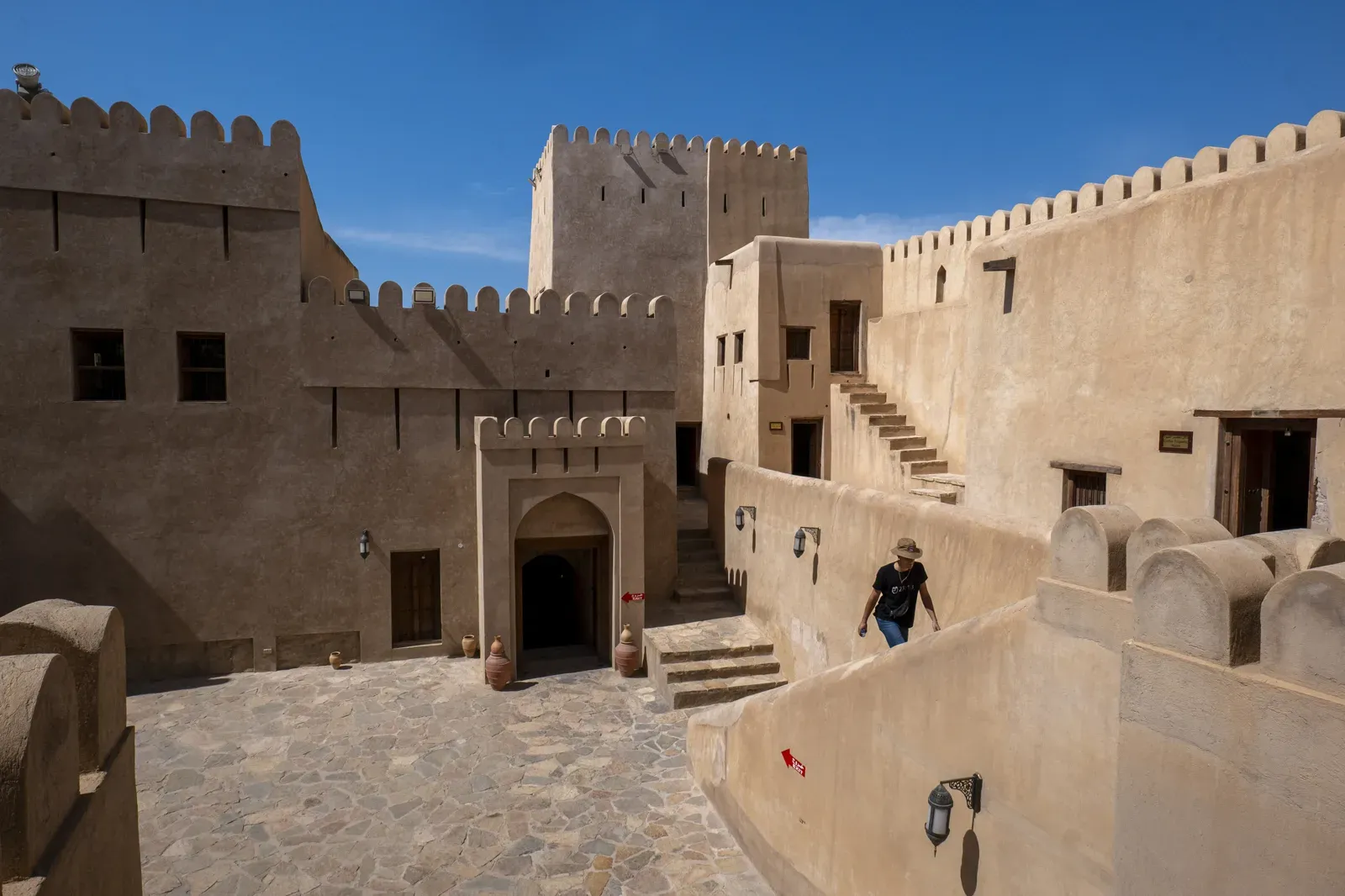 Een geplaveide binnenplaats binnen Nizwa Fort met trappen, poorten en wachttorens van zandkleurige steen