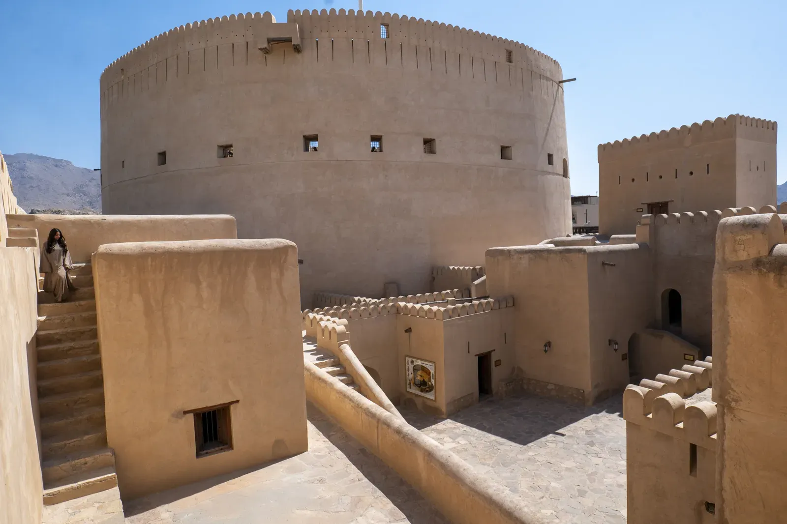 De massieve ronde verdedigingstoren van Nizwa Fort van dichtbij, met de zandkleurige muren en kantelen tegen een blauwe lucht