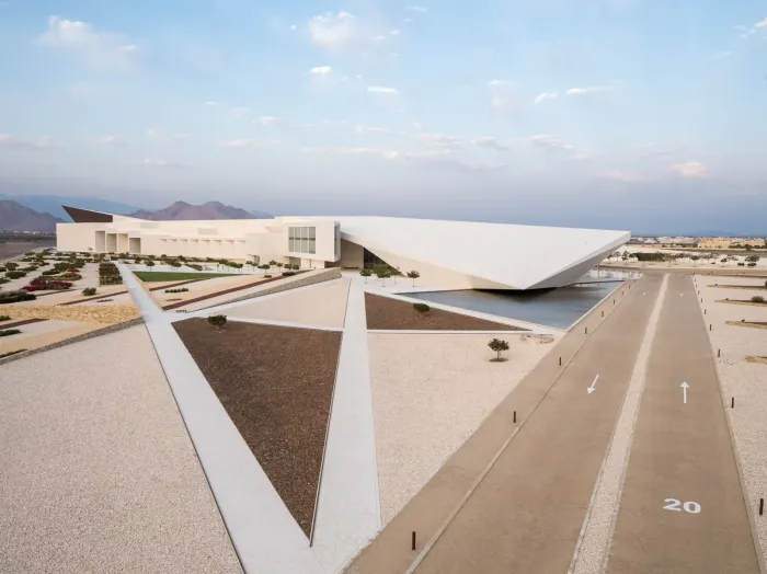 Het strakke, hoekige witte gebouw van het Oman Across Ages Museum in Manah met de Hajar-bergen op de achtergrond