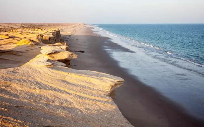Door de wind gevormde zandsteenkliffen die uitlopen in een lang strand langs de Arabische Zee bij Ras Ar Ruways