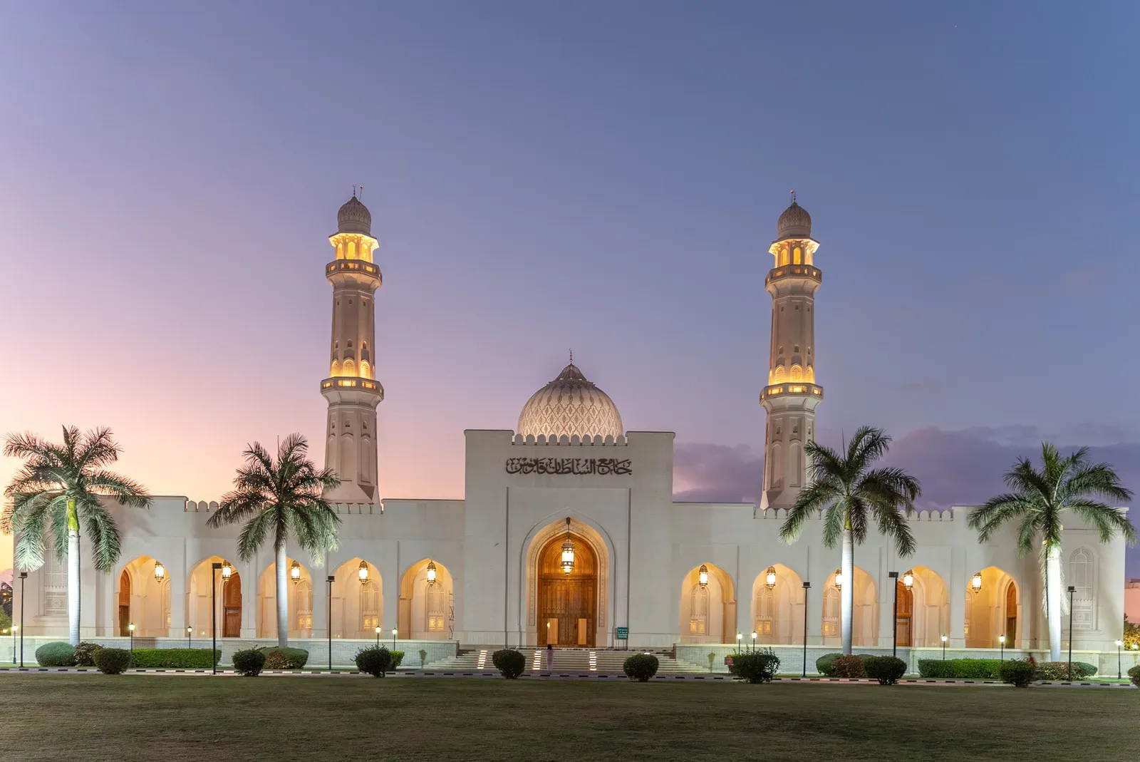De verlichte Sultan Qaboos-moskee van Salalah met palmen bij avondschemering