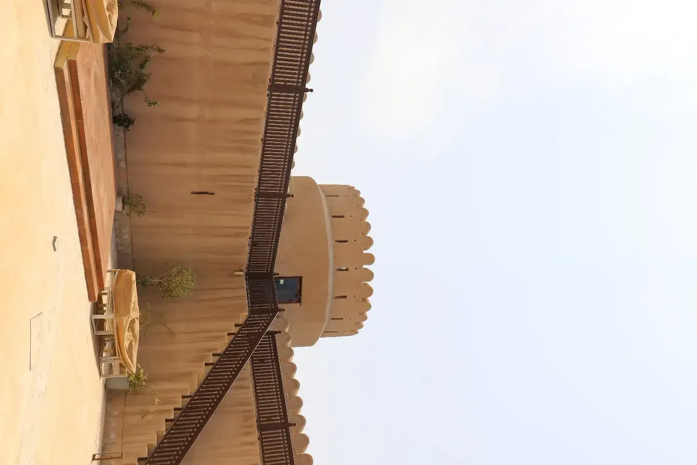 De binnenplaats van Sur Burj al Khamis met een houten trap langs de muur die naar de ronde centrale toren leidt
