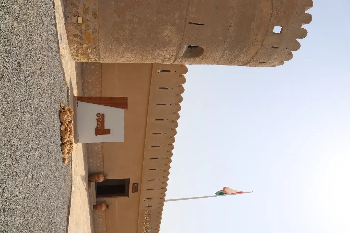 De entree van Sur Burj al Khamis met de ronde hoektoren, gekanteelde muur en de Omaanse vlag aan de mast
