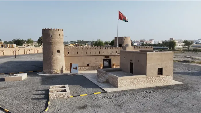 Luchtfoto van het gerestaureerde fort Sur Burj al Khamis met ronde toren, vestingmuur en de Omaanse vlag onder een heldere lucht