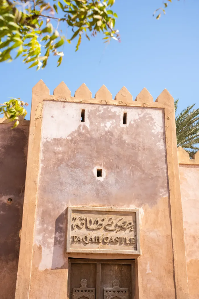 De poort van Taqah Castle met een gebeeldhouwd naambord boven de houten deur