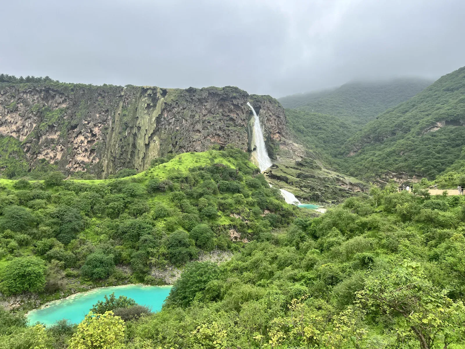 De waterval en turquoise poelen van Wadi Darbat tussen weelderig groene, in mist gehulde berghellingen