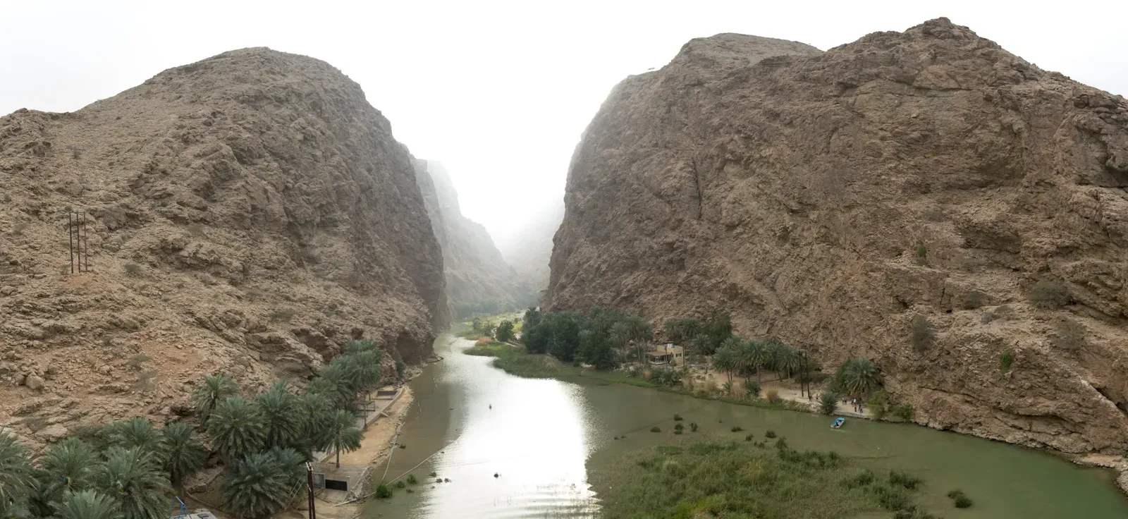 Panorama van de brede kloof van Wadi Shab met de groene rivierbedding tussen hoge, kale bergwanden